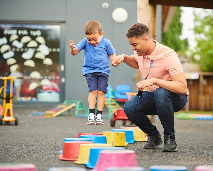 Physical Activity for Positive Behavior Support A teacher helping a child jump through a colorful stepping stones course on an outdoor playground.