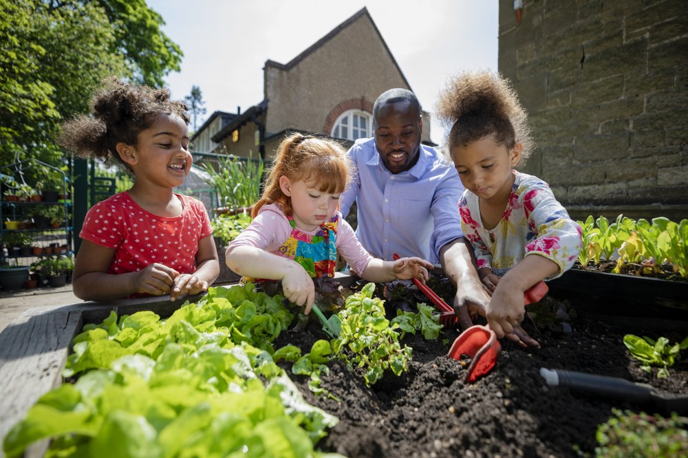 Use the Head, Heart, and Hands (and Green Muscle Memory!) to Love and Care for Nature Adult with young children working in a garden outside